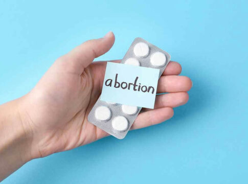 Hand holding pills labeled abortion on blue background.