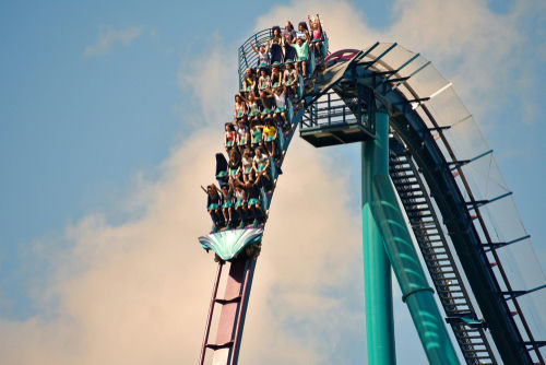 Roller coaster plunging down a steep drop with riders raising their hands