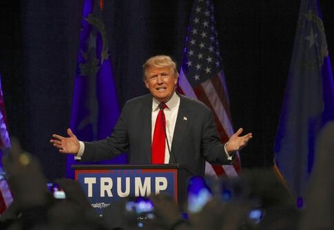 A speaker gesturing passionately at a political rally with American flags in the background