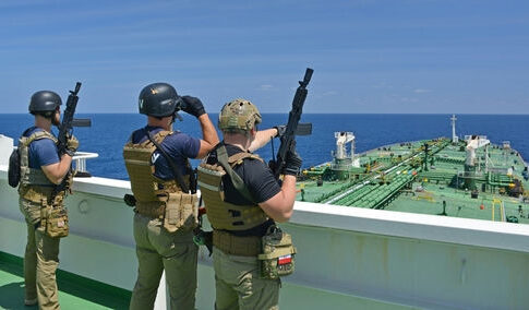 Armed security team on a ship deck overlooking a large tanker at sea